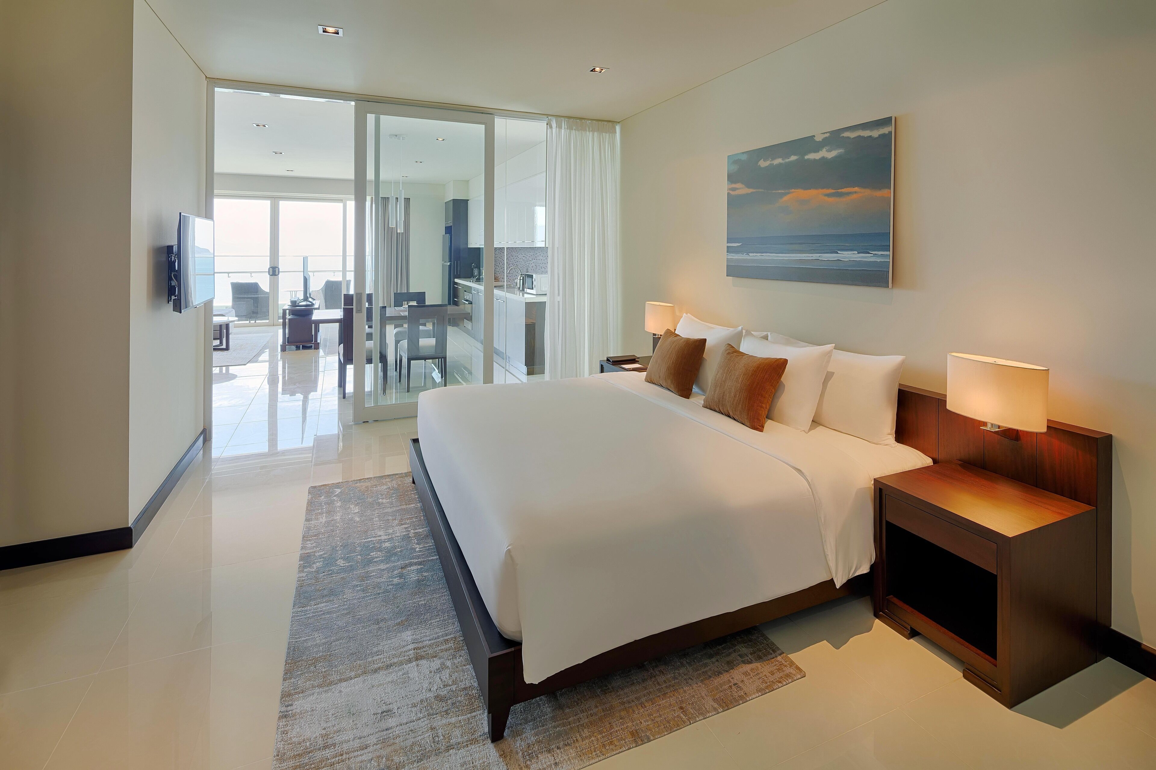 Habitación de hotel moderna con una cama grande, un escritorio, una silla, un televisor y vistas al océano a través del ventanal.