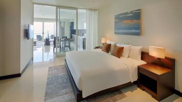 Habitación de hotel moderna con una cama grande, un escritorio, una silla, un televisor y vistas al océano a través del ventanal.