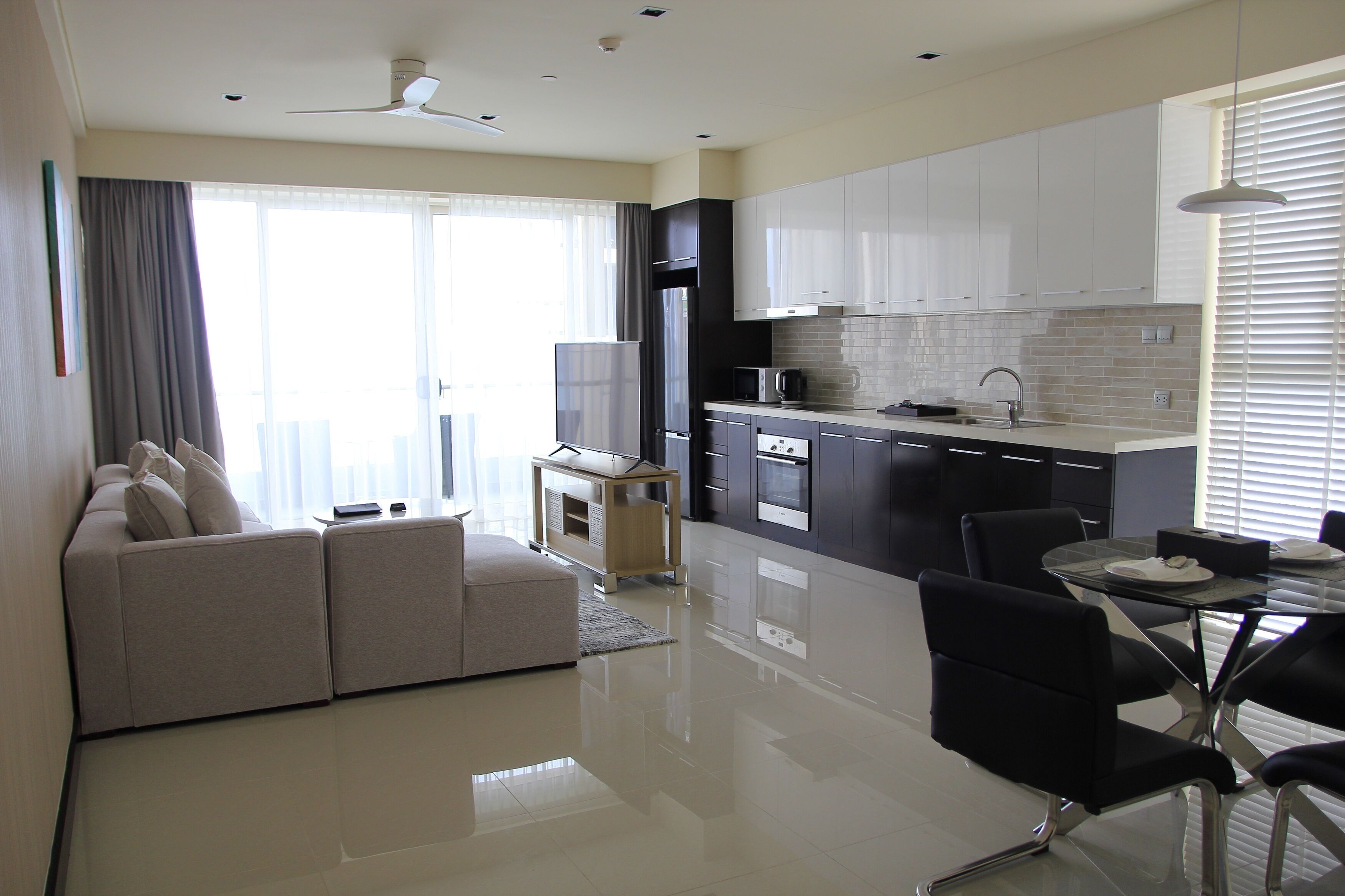 A modern kitchen with white cabinets, a dining table with chairs, and a sofa in a living area.