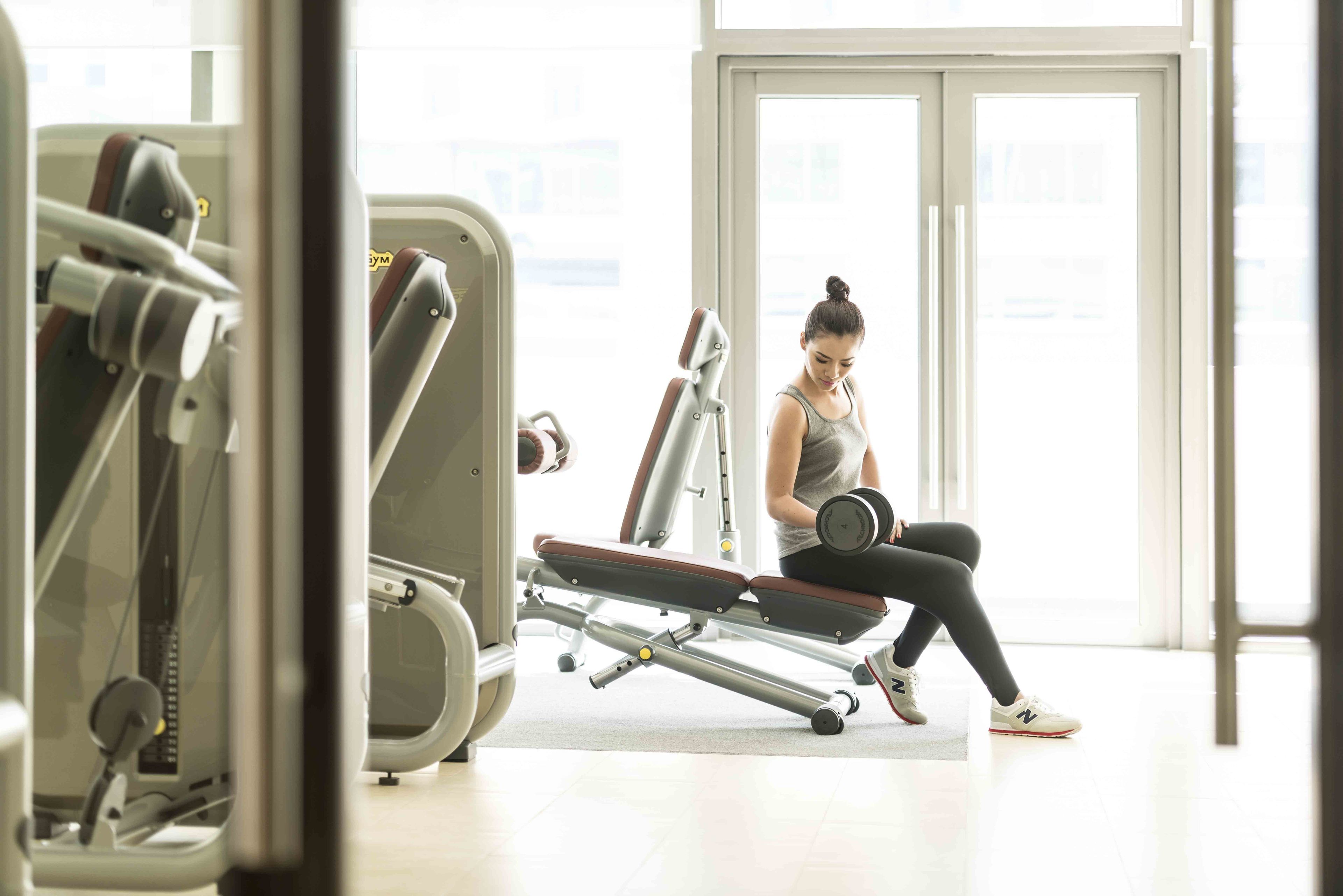 A gym with exercise equipment and a person using a dumbbell.