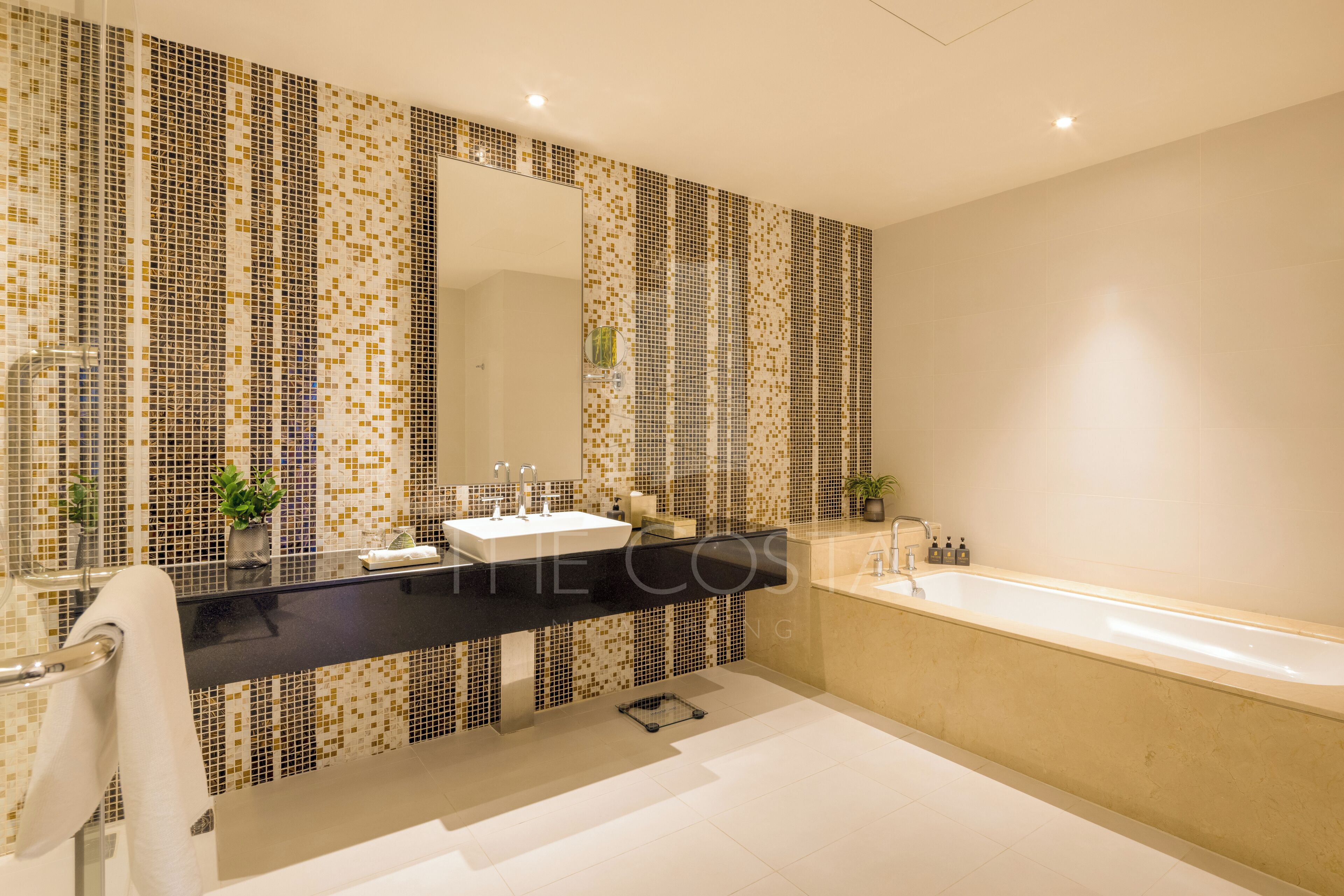 A modern bathroom with a black countertop, a white sink, and a beige bathtub.