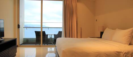 Un cuarto de hotel con una cama grande, televisión, balcón con mesa y sillas, y vista al mar.
