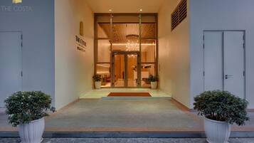 A hotel entrance with a modern design, featuring a glass door, a wooden ceiling, and potted plants on either side.