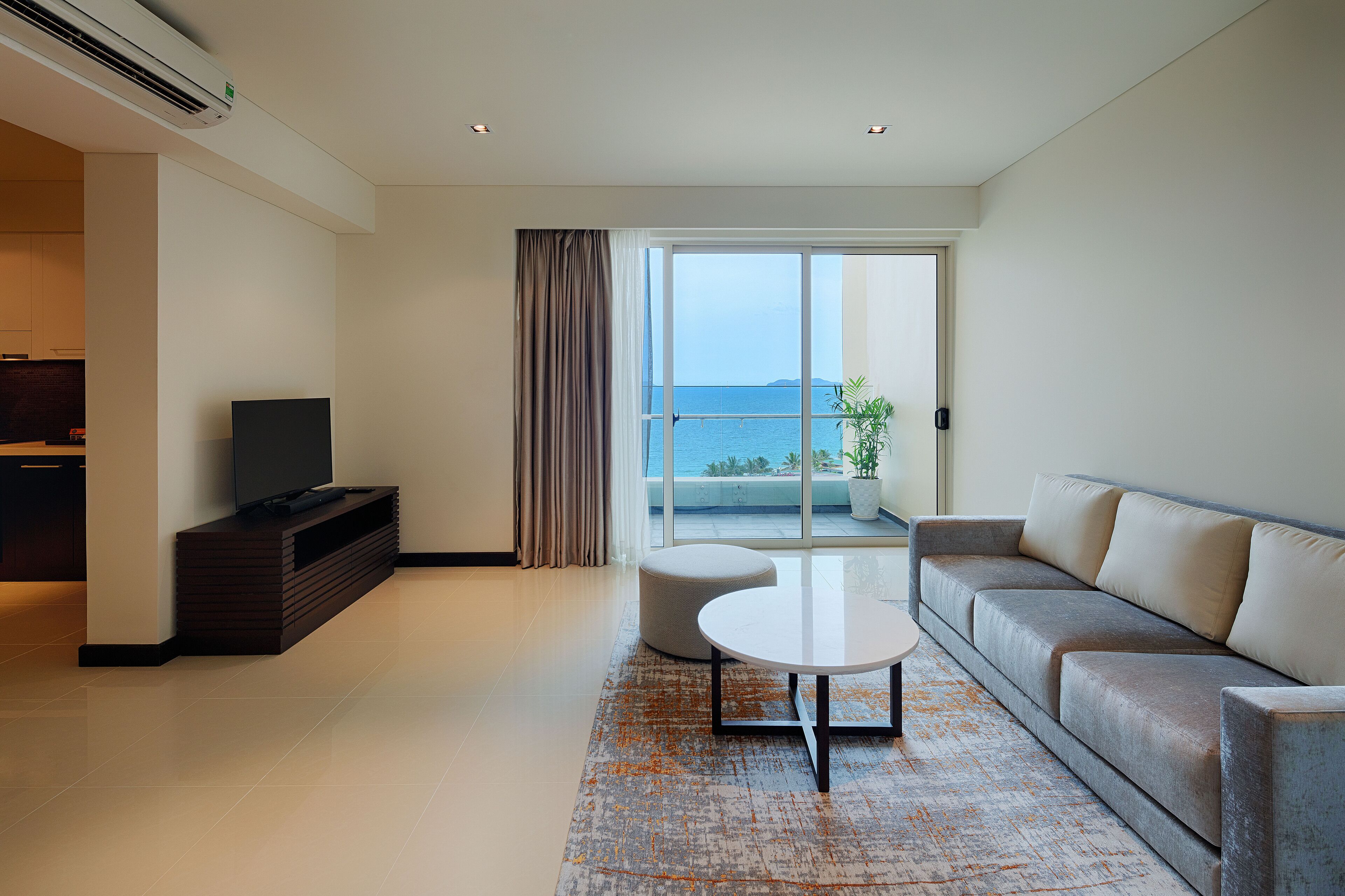 Una sala moderna con televisor de pantalla plana, un sofá, una mesita redonda y vistas al mar a través de amplios ventanales.