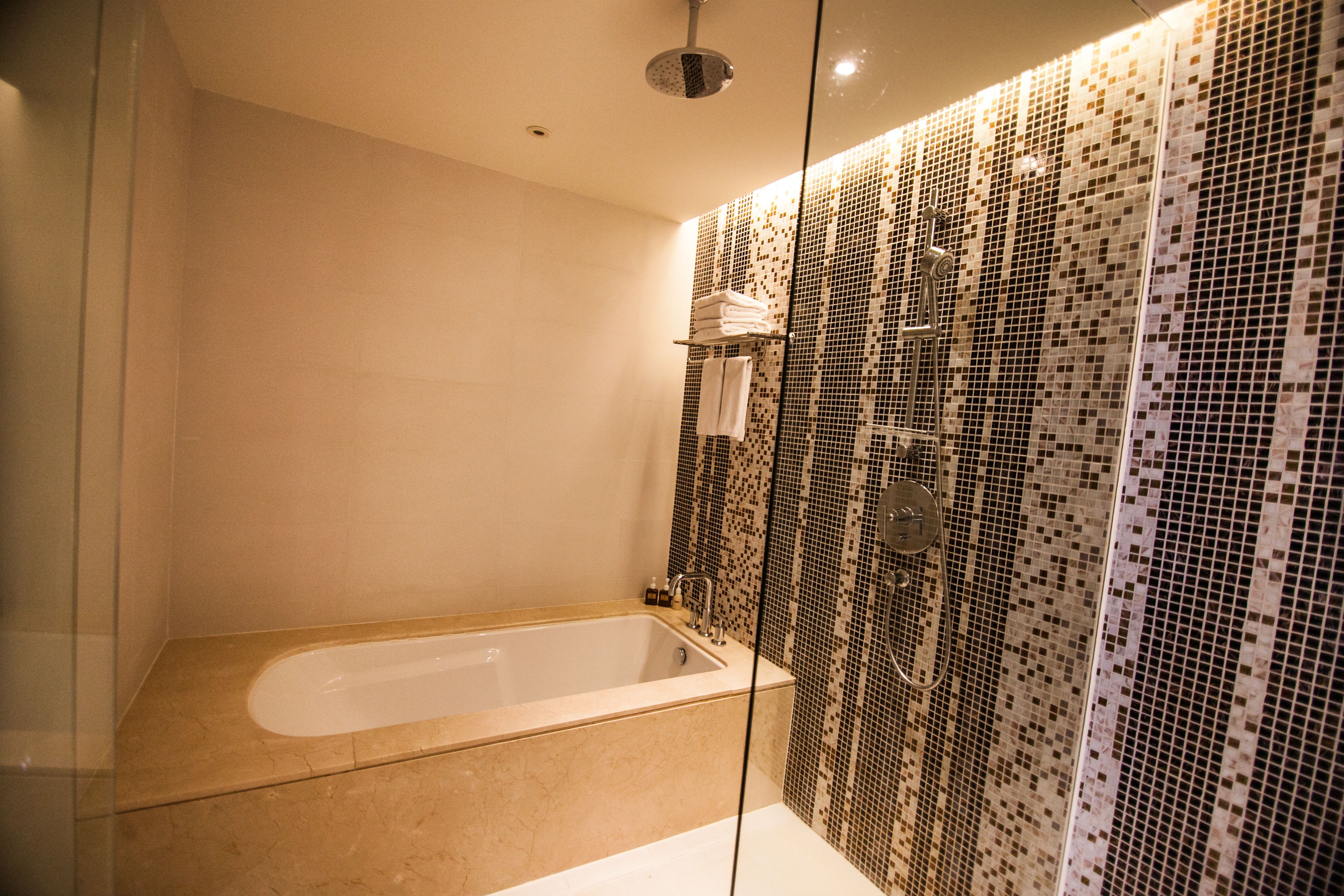A modern bathroom with a freestanding bathtub, a glass-enclosed shower area, and a tiled mosaic wall.