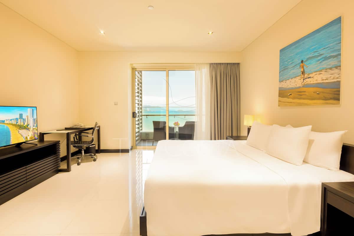 Hotelkamer met een bed, bureau, stoel, televisie, schilderij en uitzicht op zee.