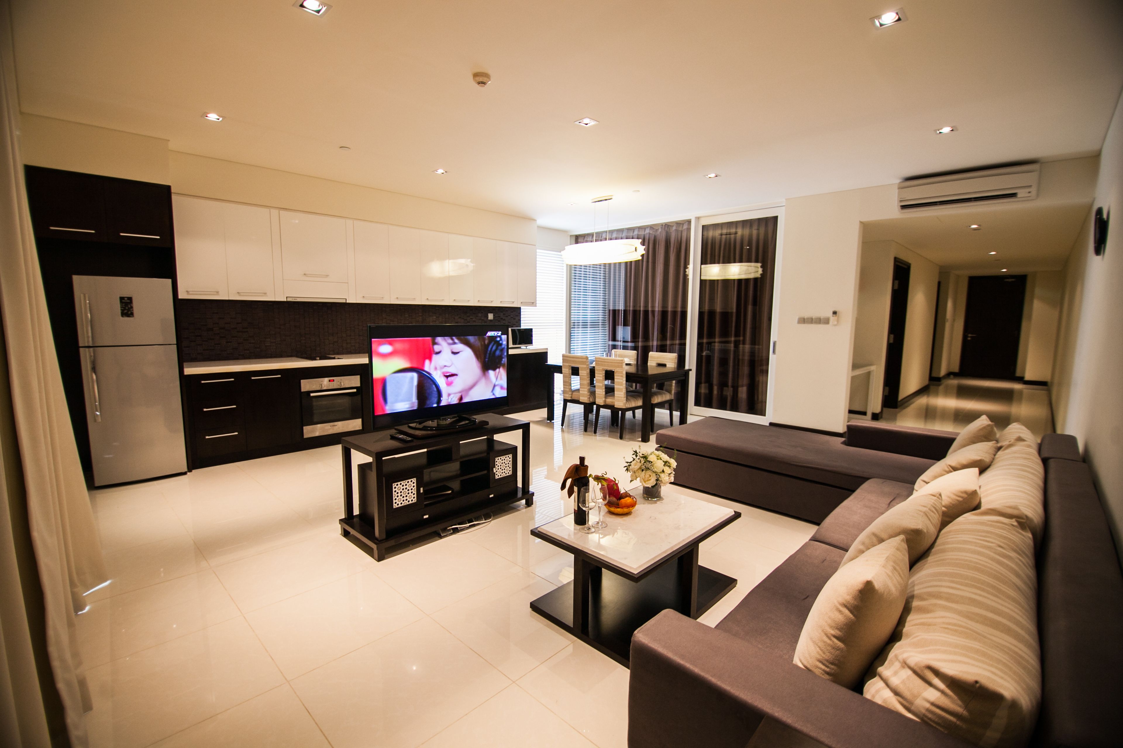 A modern living room with a flat-screen TV, a sofa, a coffee table, and a dining area with a table and chairs.
