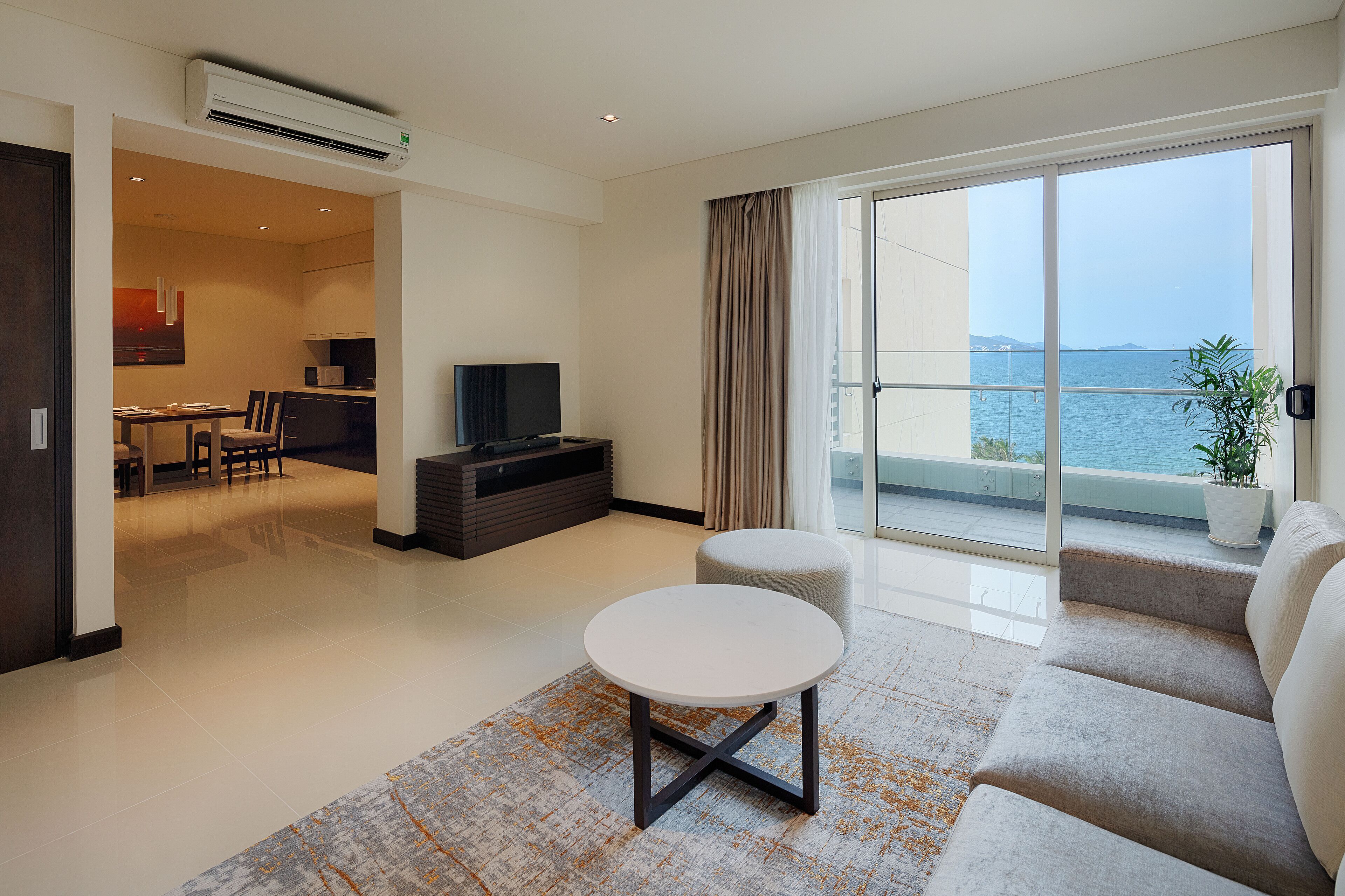 Un salon moderne avec un canapé, une table ronde et un téléviseur. Il y a un balcon avec vue sur la mer.