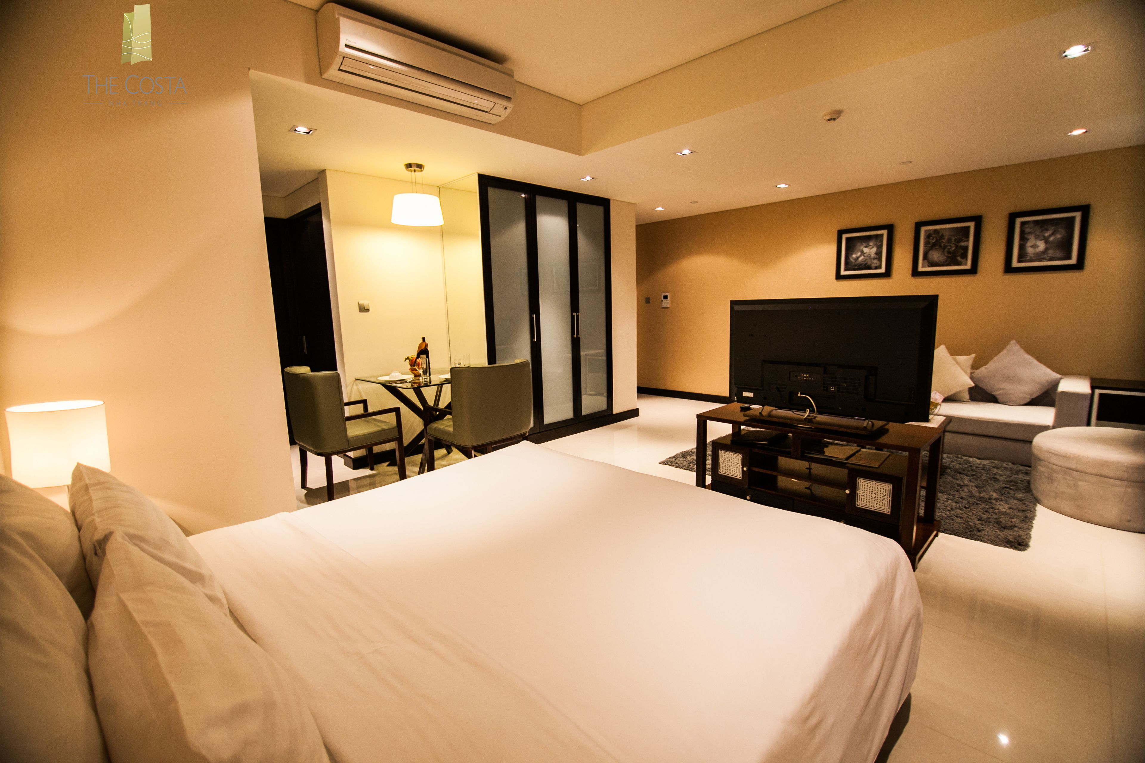 A hotel room with a large bed, a desk with a chair, a television, and a sofa.