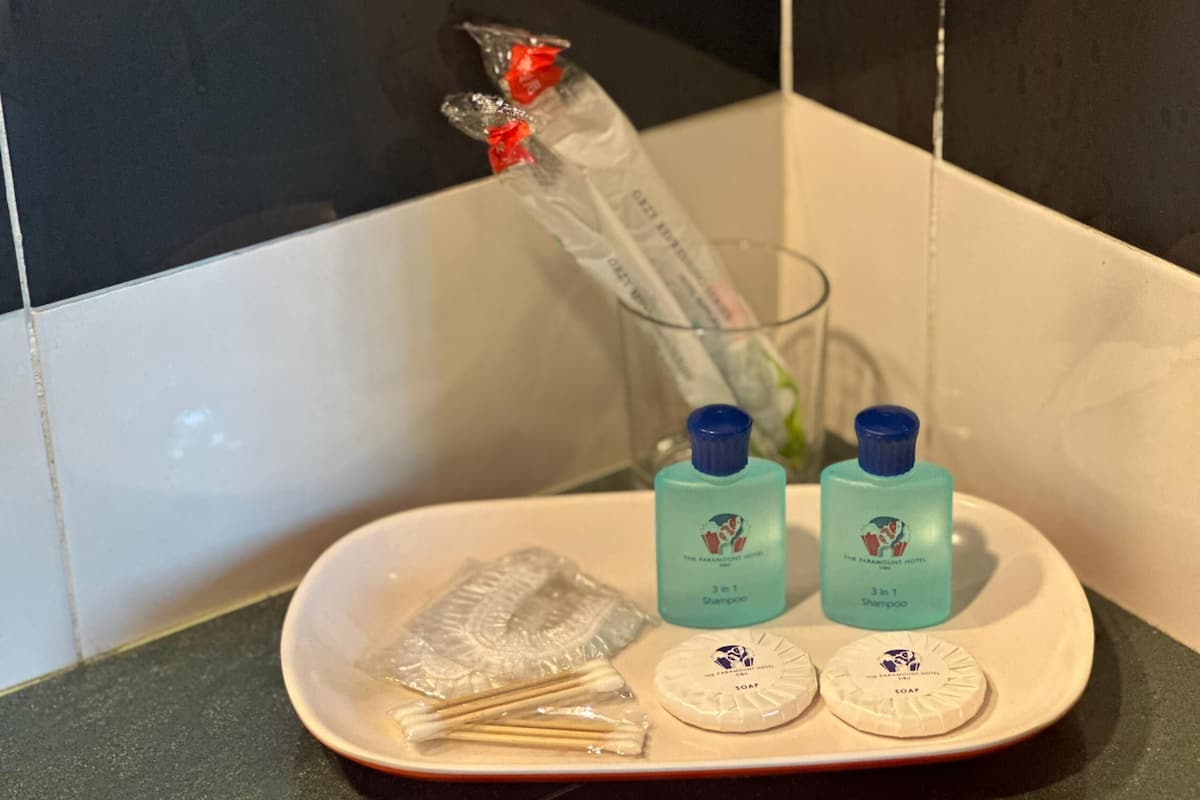 A bathroom counter with toiletries including two bottles of shampoo, two soap bars, and a glass with a toothbrush.