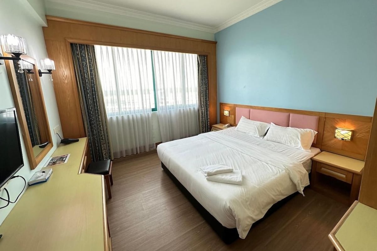 Habitación de hotel con una cama grande, mesitas de noche, un escritorio con televisor de pantalla plana y un ventanal con cortinas.