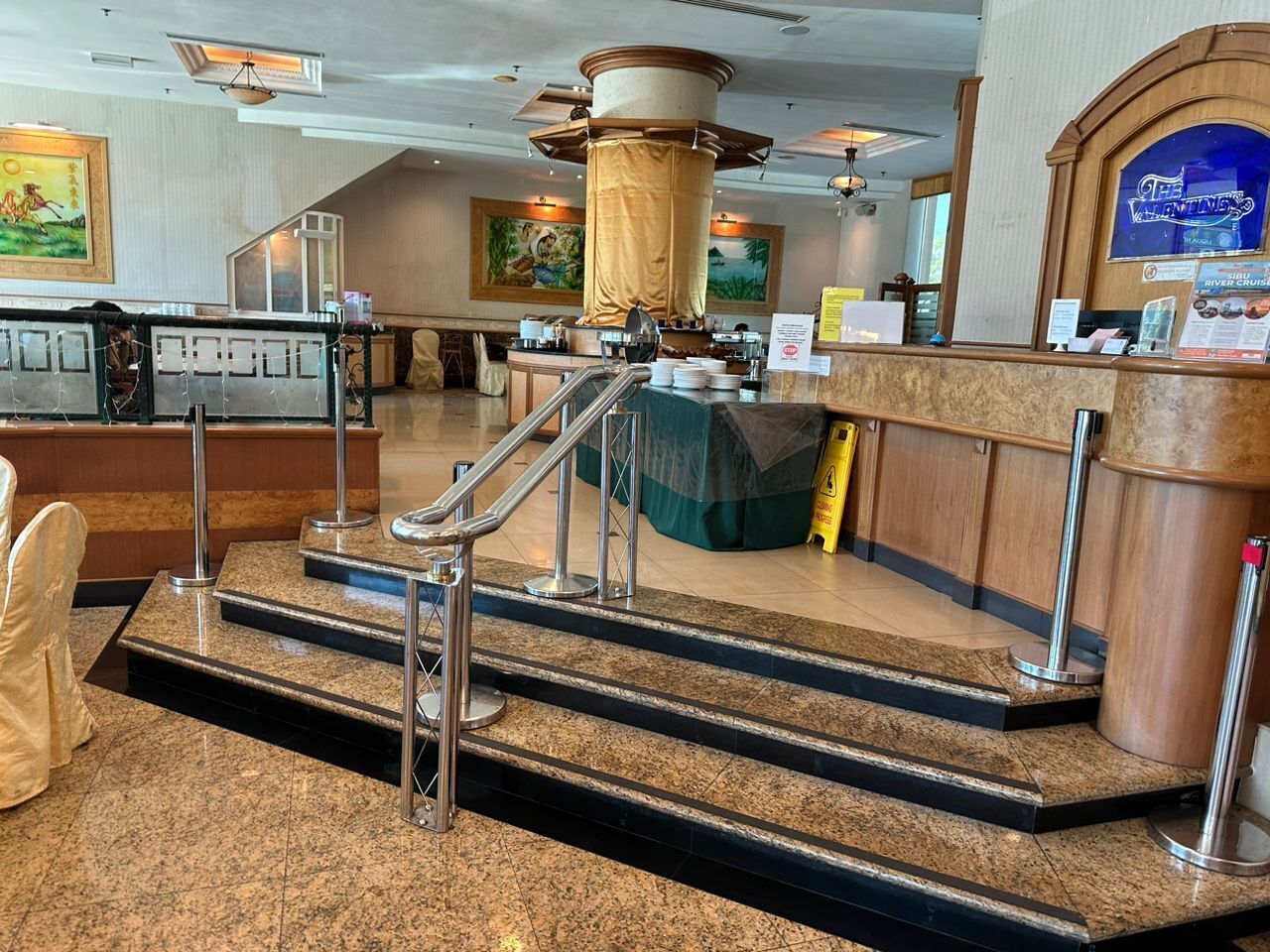 A hotel lobby with a reception desk, a staircase, and a large pillar.