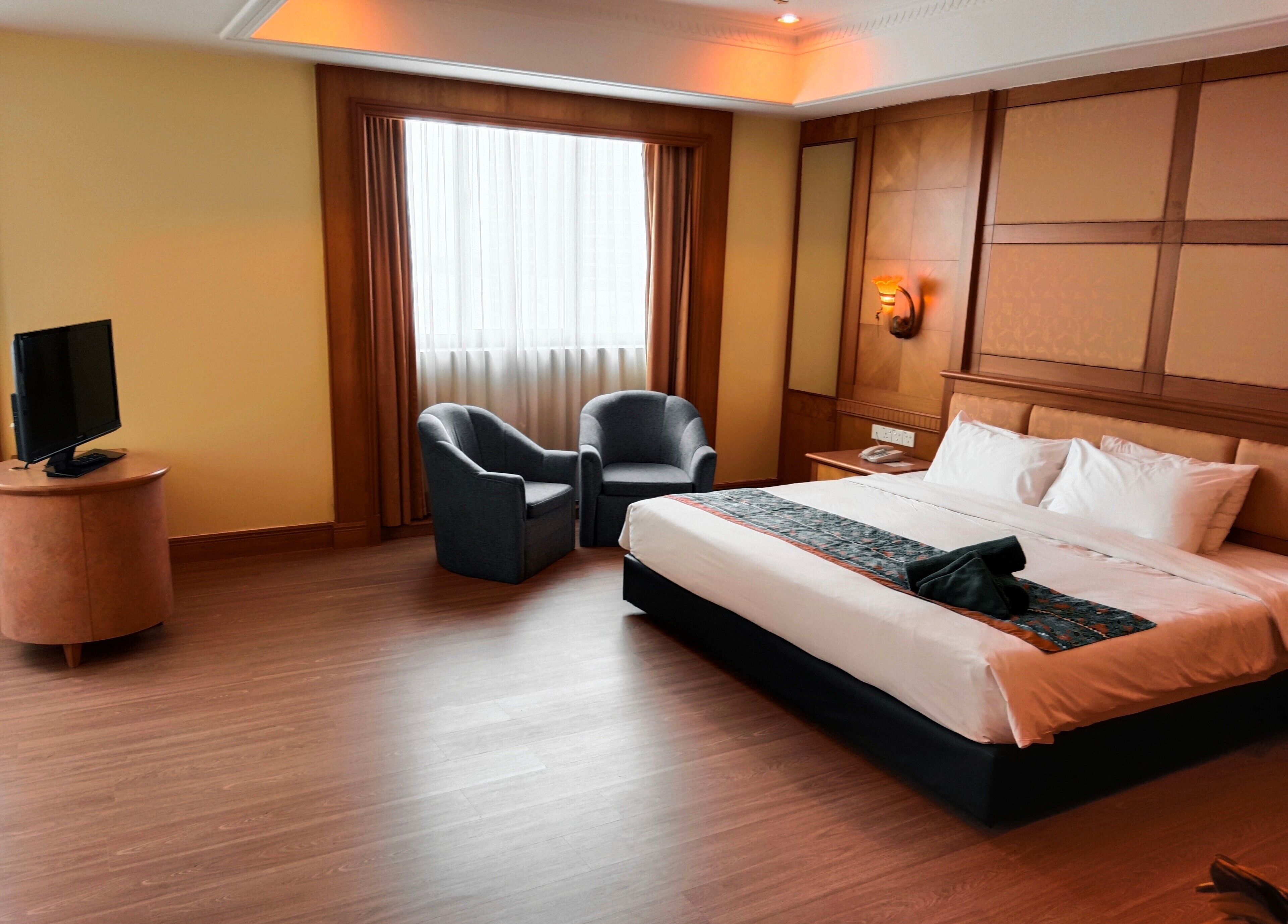 A hotel room with a bed, two armchairs, a desk with a lamp, and a television on a stand.