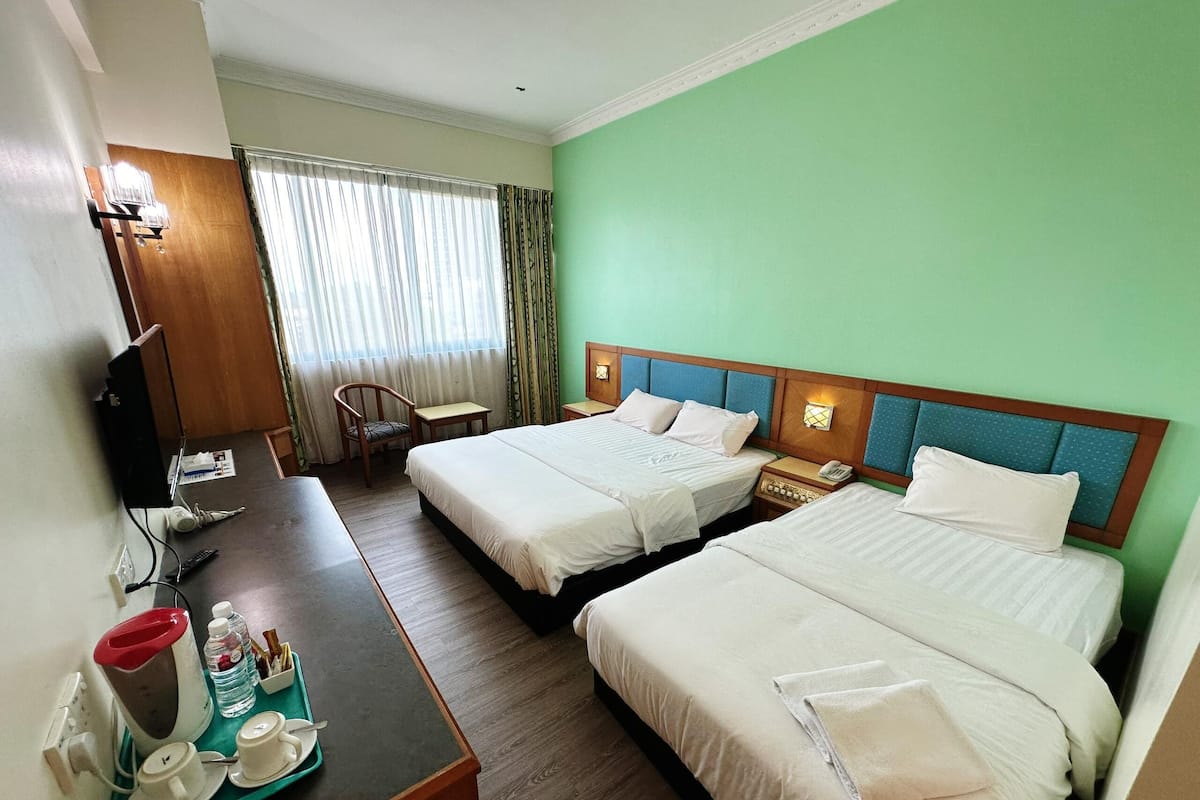A hotel room with two beds, a desk with a tray of toiletries, a chair, and a television.