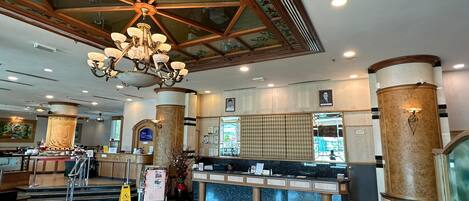 A hotel lobby with a reception desk, a chandelier, and a large window.