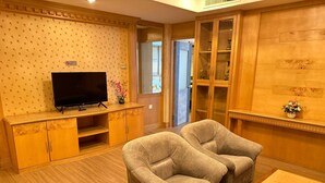 Una sala de estar con televisor, dos sillones, un aparador de madera y una mesita.
