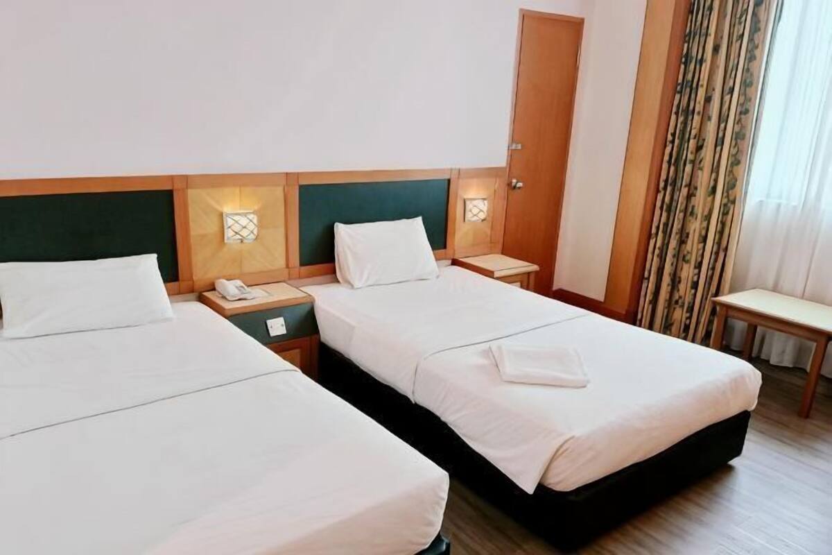 A hotel room with two beds, bedside tables, a chair, and a door.