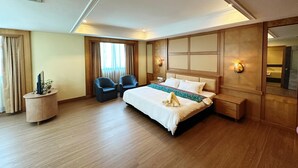 Una habitación de hotel con una cama grande, dos sillones, una mesita de noche, un espejo y una ventana con cortinas.