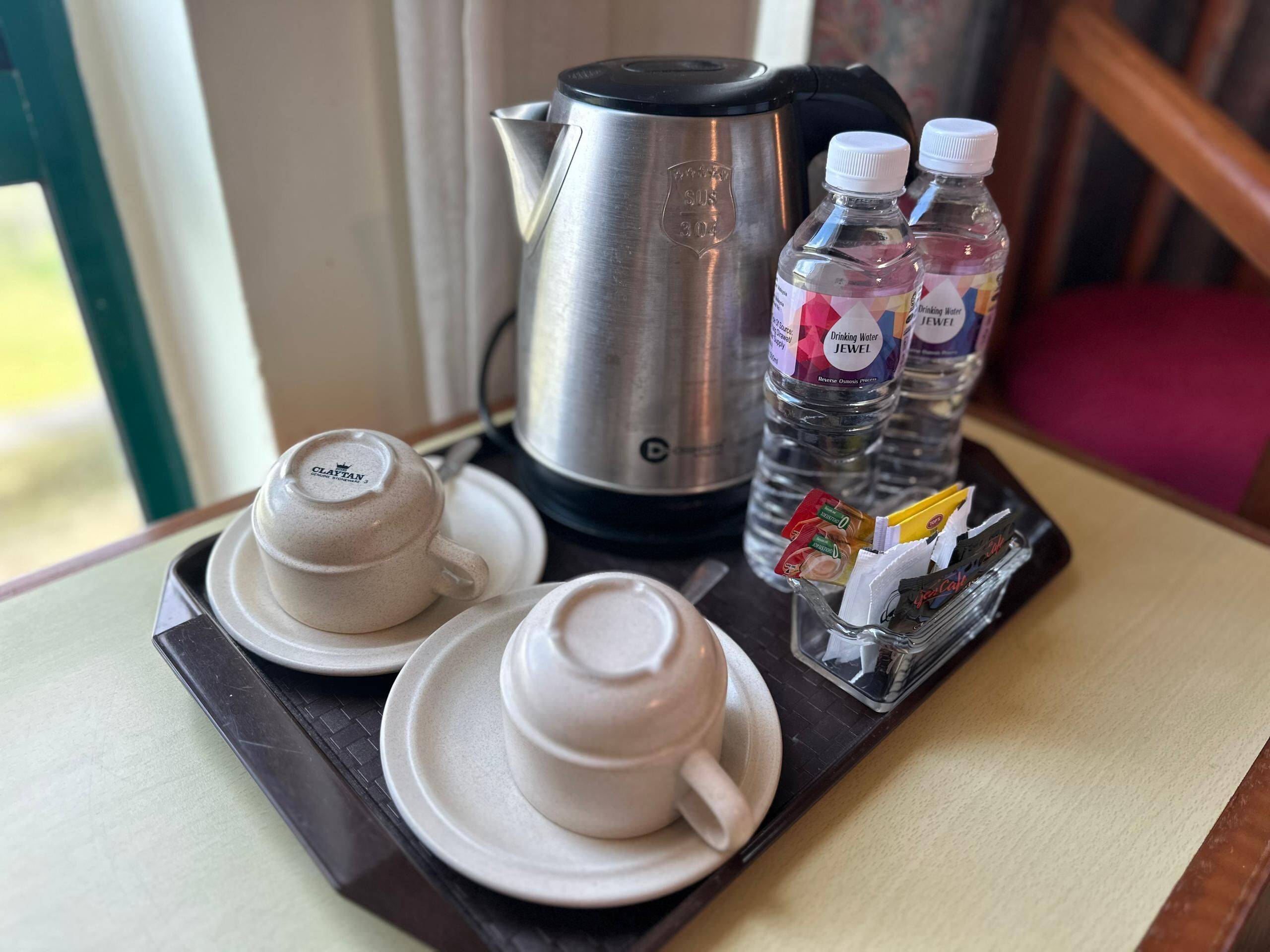 A tray with a coffee pot, two cups of coffee, and two water bottles on a table.