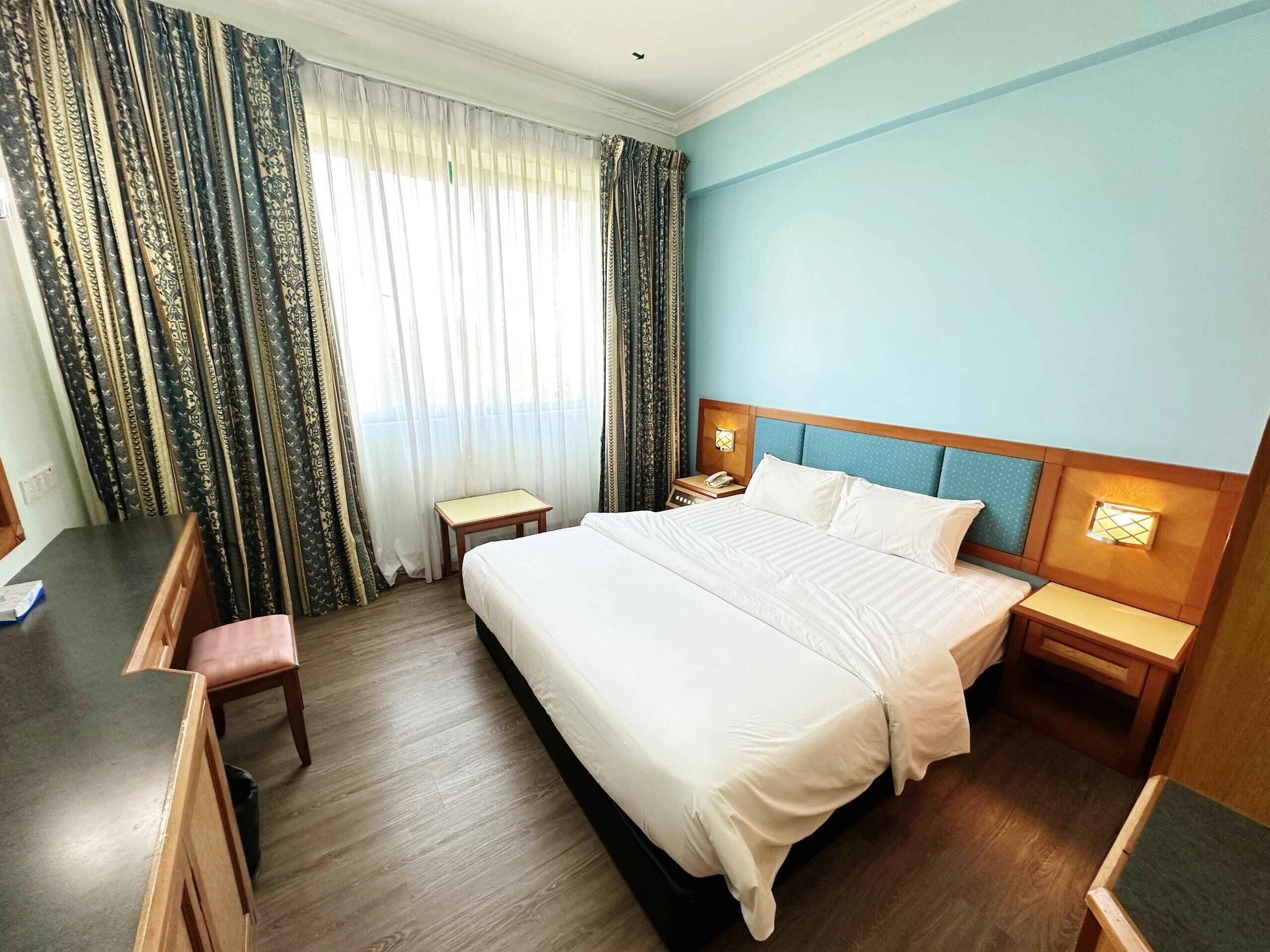 A hotel room with a large bed, two bedside tables, a desk, and a chair.