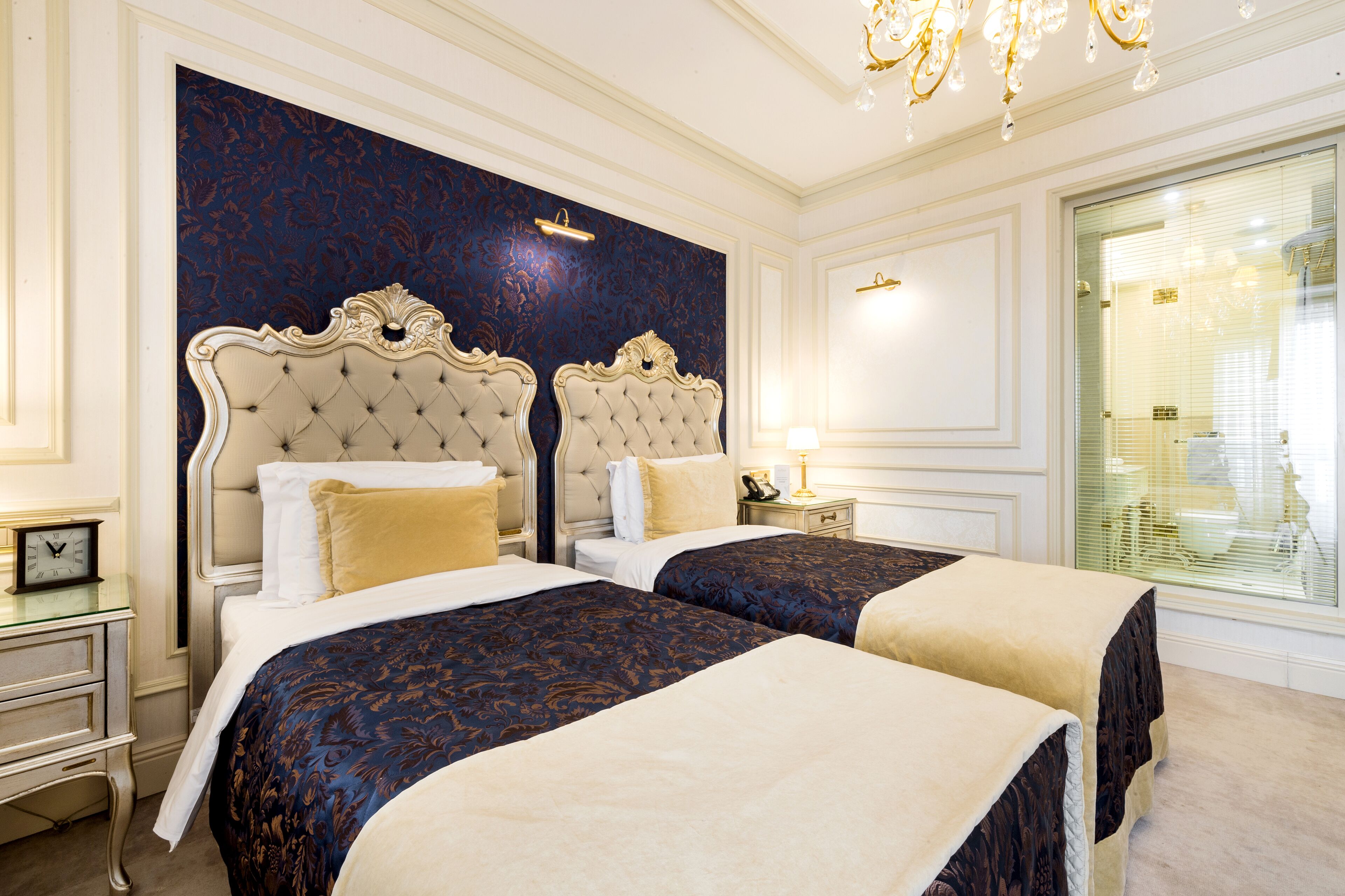 Ein Hotelzimmer mit zwei Betten, einer Kandelaber und einem großen Fenster mit Jalousien.
