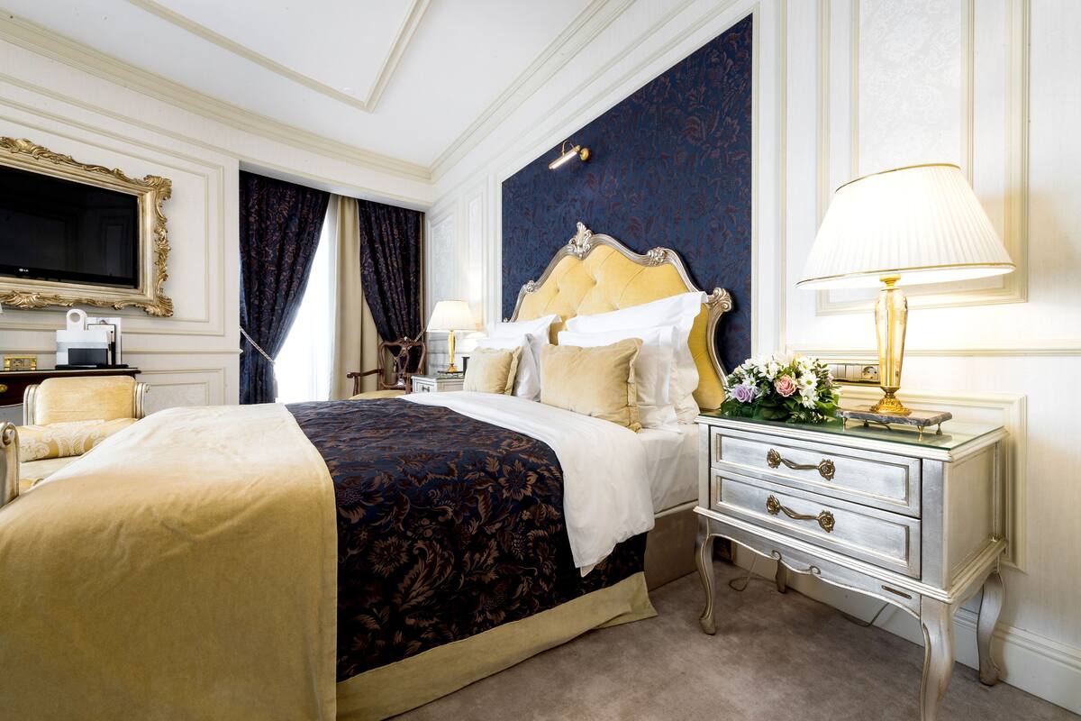 A luxurious bedroom with a large bed, a nightstand with a lamp, a dresser, and a television on the wall.