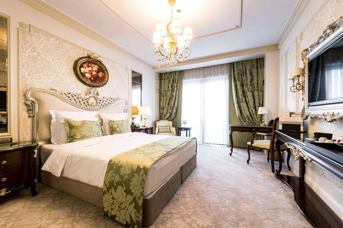 A spacious bedroom with a large bed, a vanity, a desk, and a television.
