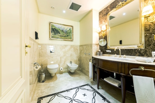 A bathroom with a marble floor, a large mirror, a sink, a bidet, and a toilet.