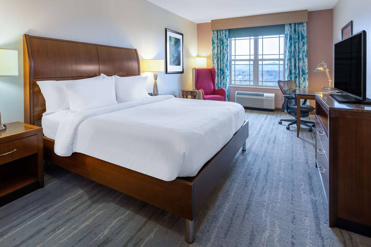 A hotel room with a large bed, a desk with a computer, a TV, and a chair.