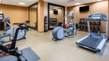 A gym with cardio machines, weight racks, and a mirrored wall.