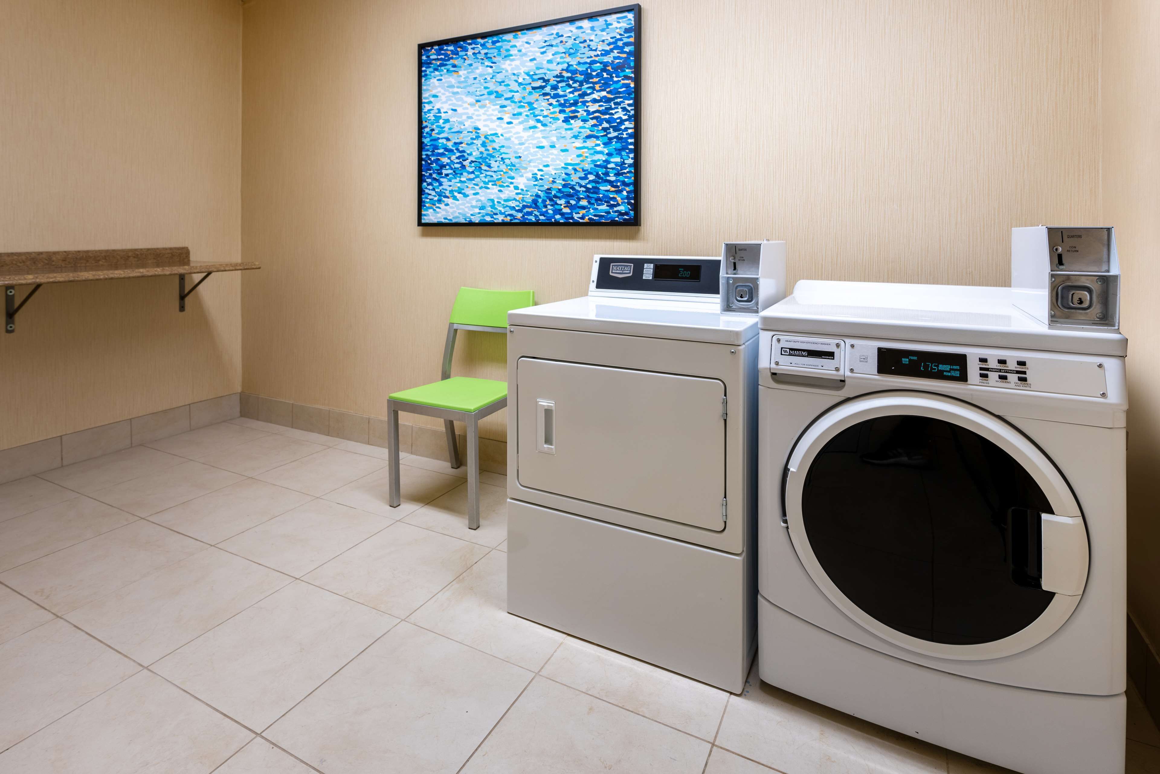 A laundry room with a washing machine, dryer, and a chair.