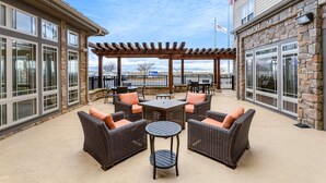 An outdoor patio area with wicker furniture and a pergola, featuring large windows and a stone building facade. - Hilton Garden Inn Roanoke (Roanoke)