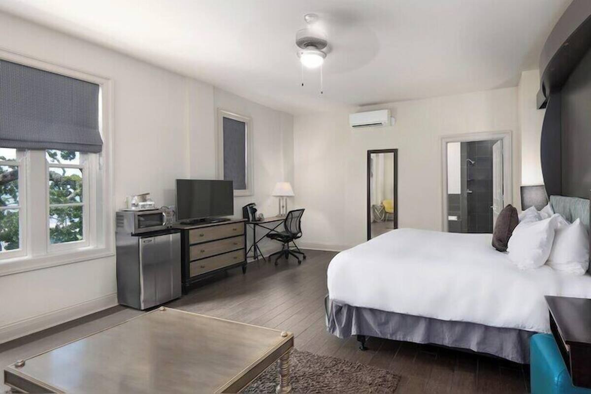 Habitación de hotel con cama, escritorio, silla, televisor y un espejo grande.