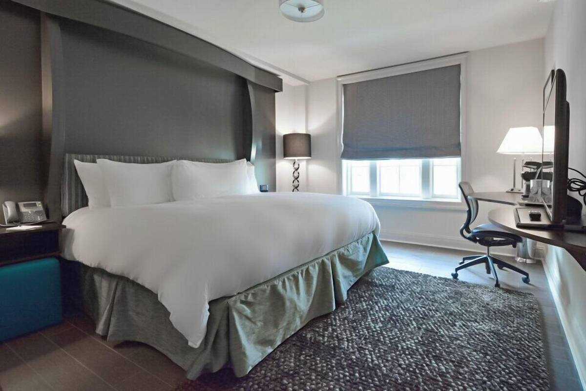 Una habitación de hotel moderna con una cama grande, un escritorio con silla, un teléfono y una ventana con persianas.