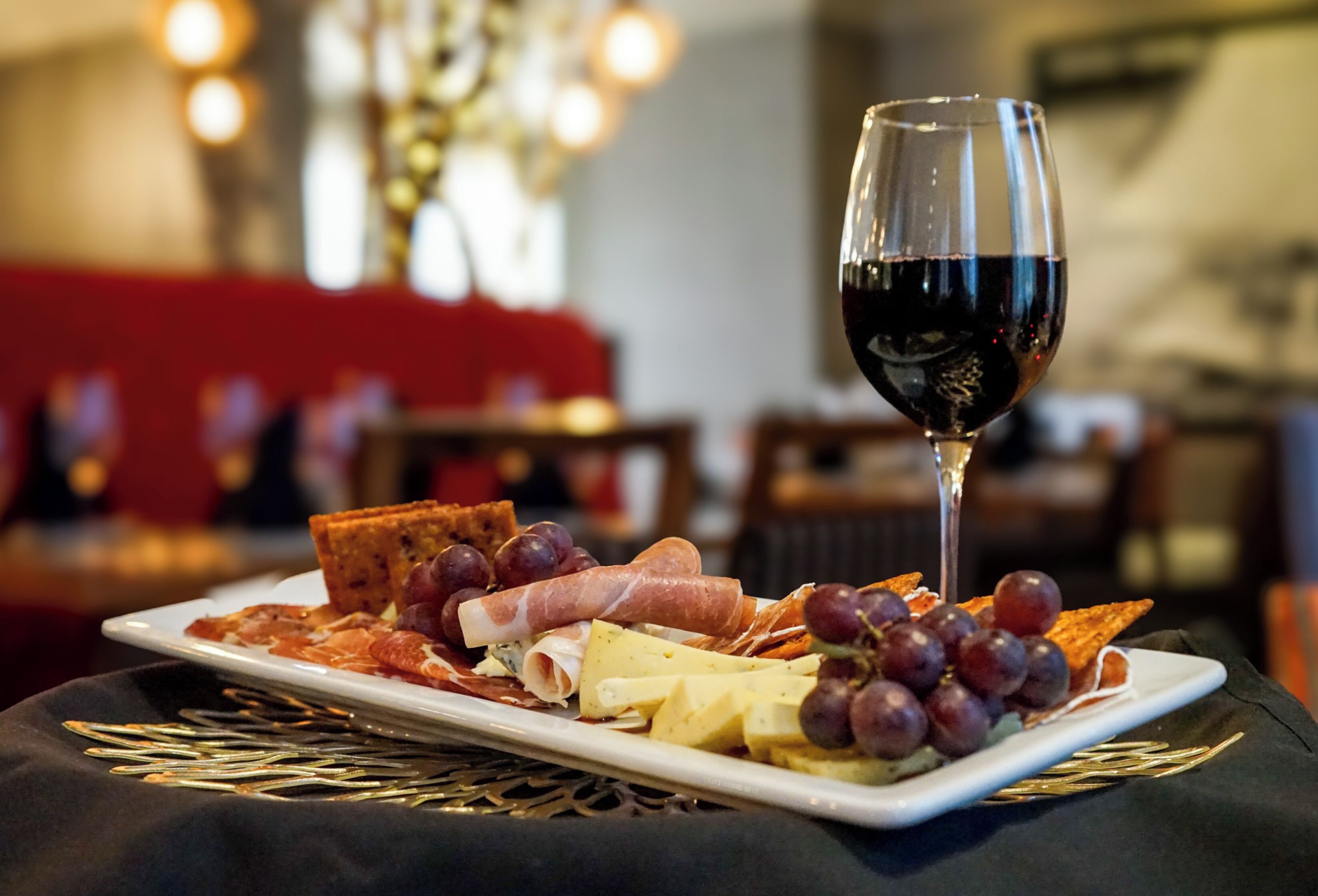 En tallerken med forskellige oste, pålæg og druer på et bord med et glas rødvin.