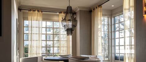 A room with a large window, a chandelier, and two white armchairs.
