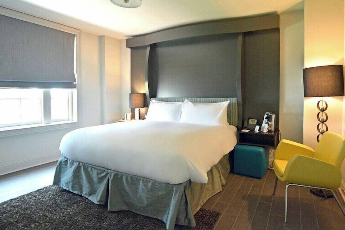 Una habitación de hotel con una cama grande, una mesita de noche, una silla y un ventanal.