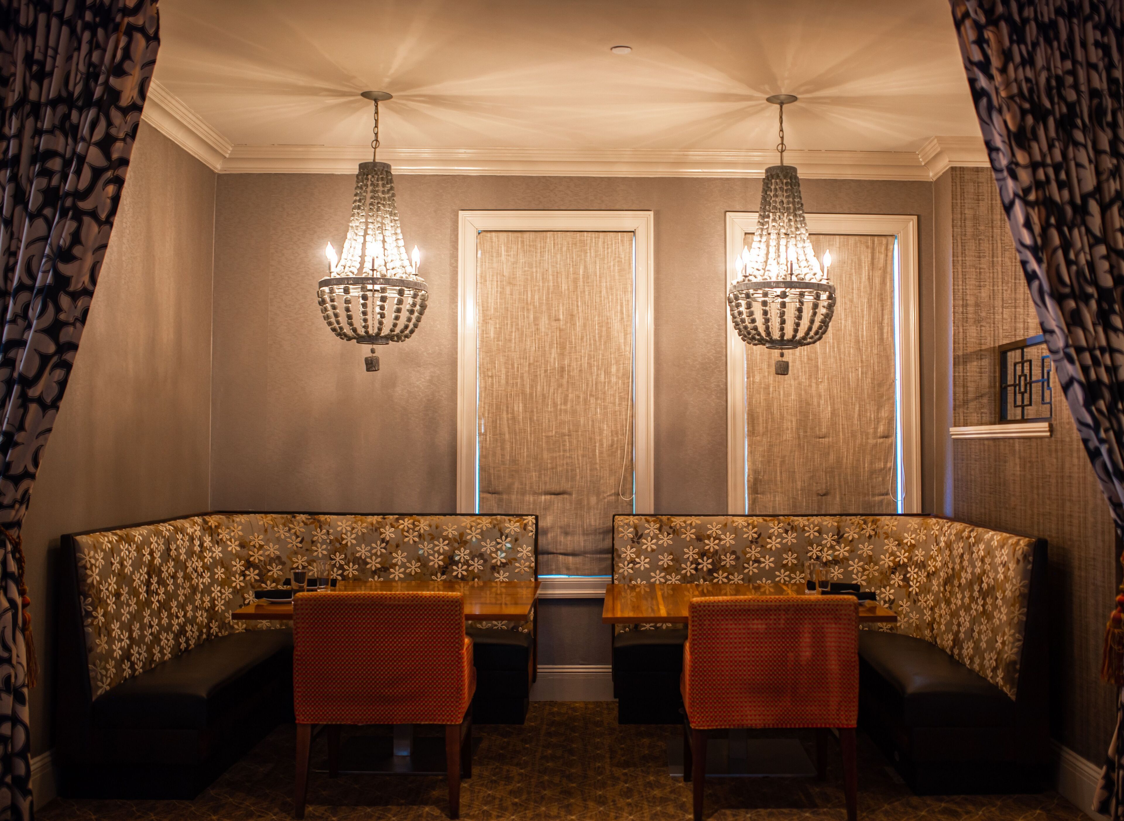 A dining area with a wooden table, two chairs, and a bench. There are two chandeliers hanging from the ceiling.