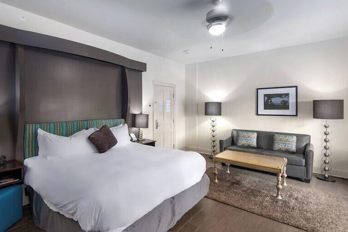 Una habitación de hotel moderna con una cama grande, un sofá, una mesa de centro y un escritorio con una lámpara.