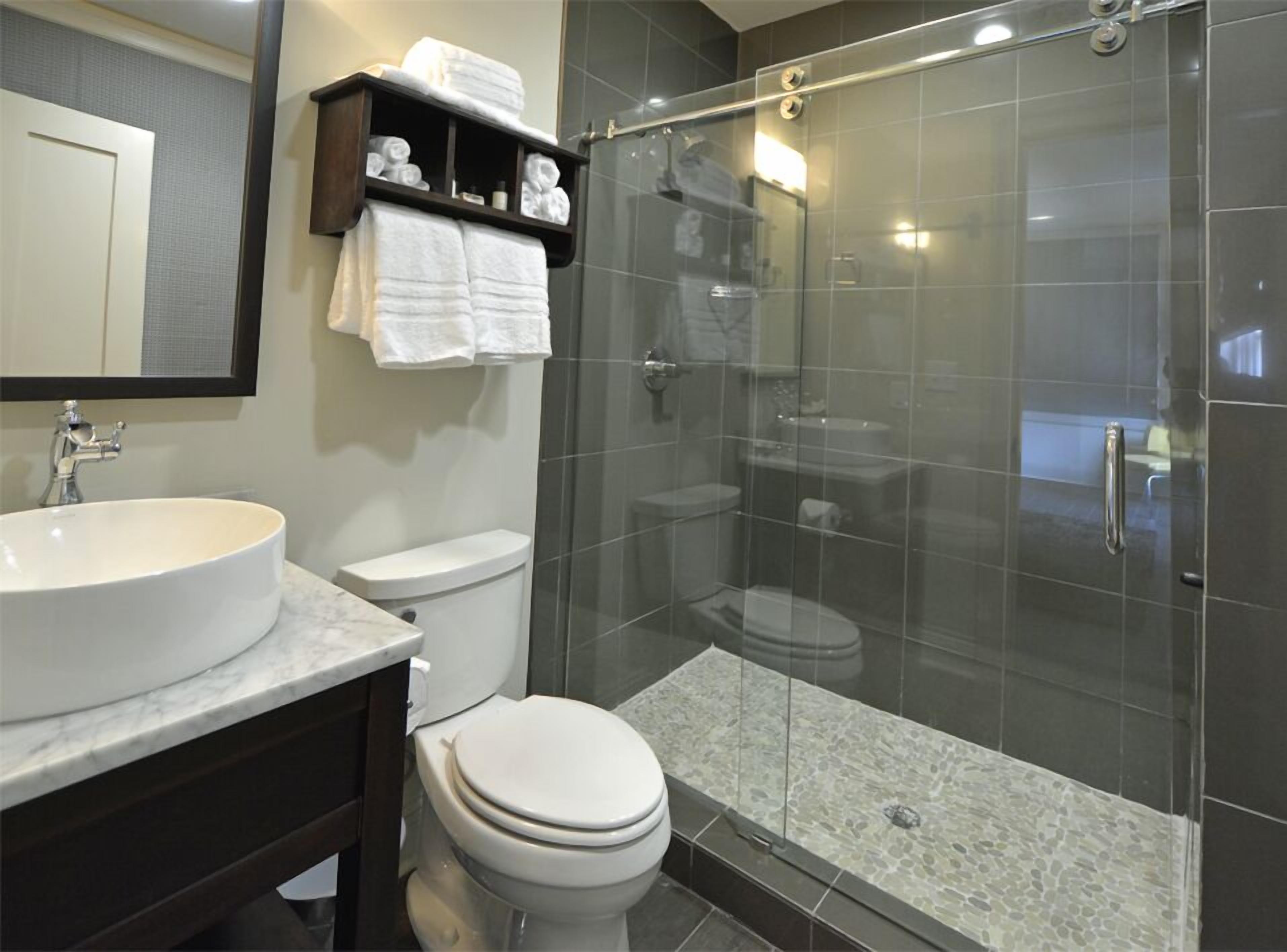 A modern bathroom with a large sink, two toilets, a glass-enclosed shower, and a towel rack.