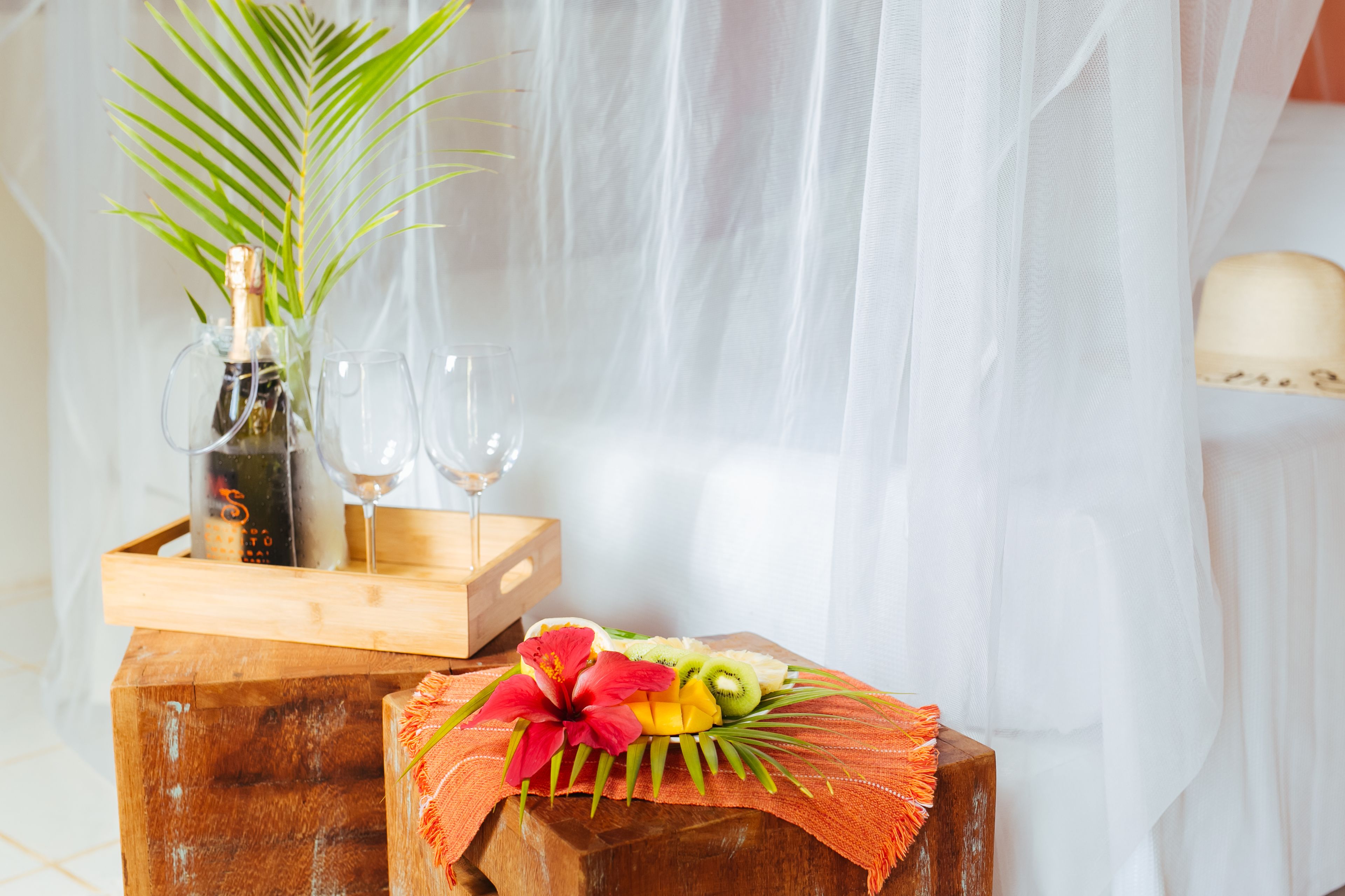 A wooden table with a bottle of champagne, two glasses, and a fruit arrangement.