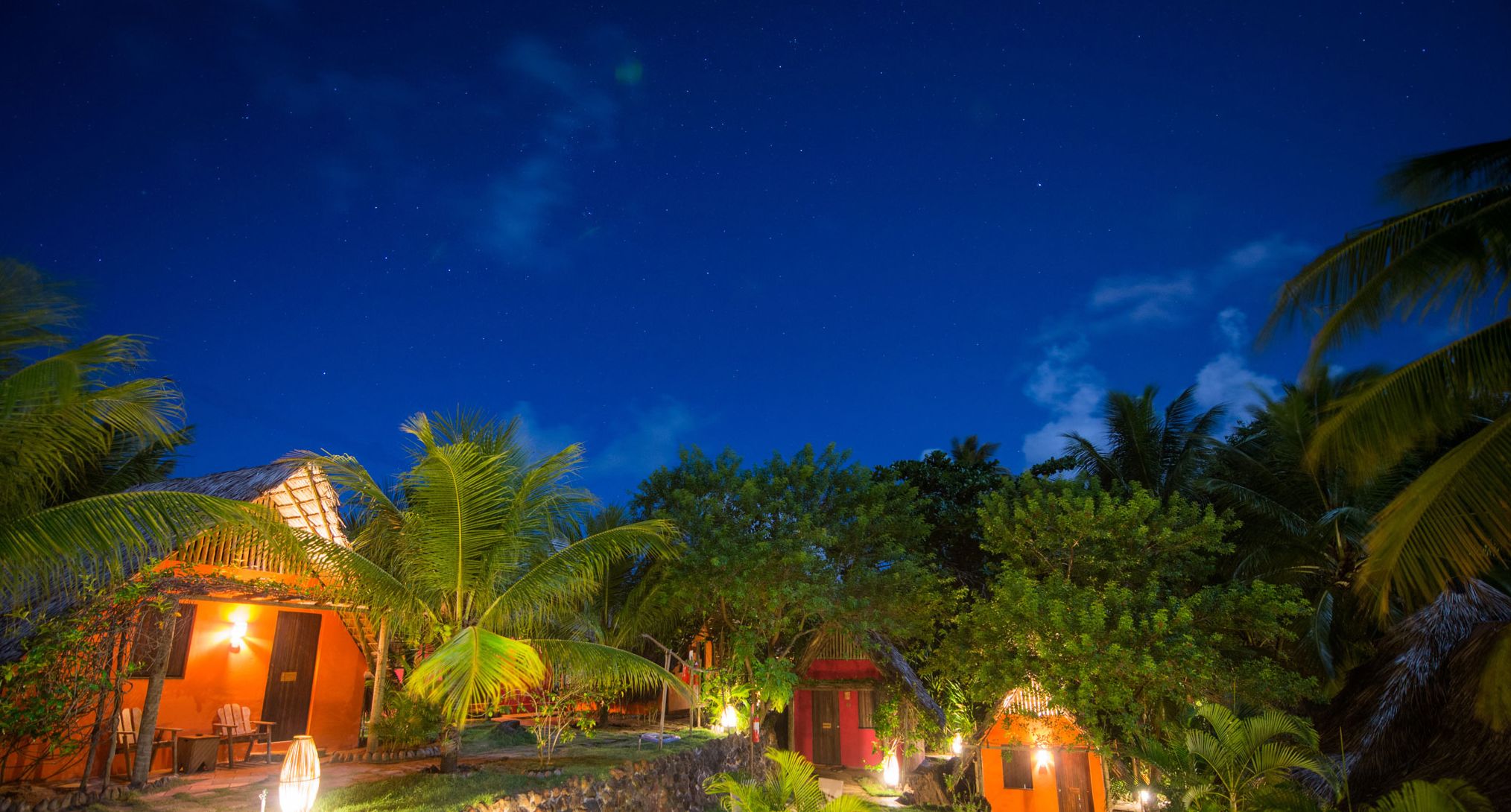 Un complexe hôtelier tropical de nuit, sous un ciel dégagé, avec des palmiers et des bâtiments illuminés.