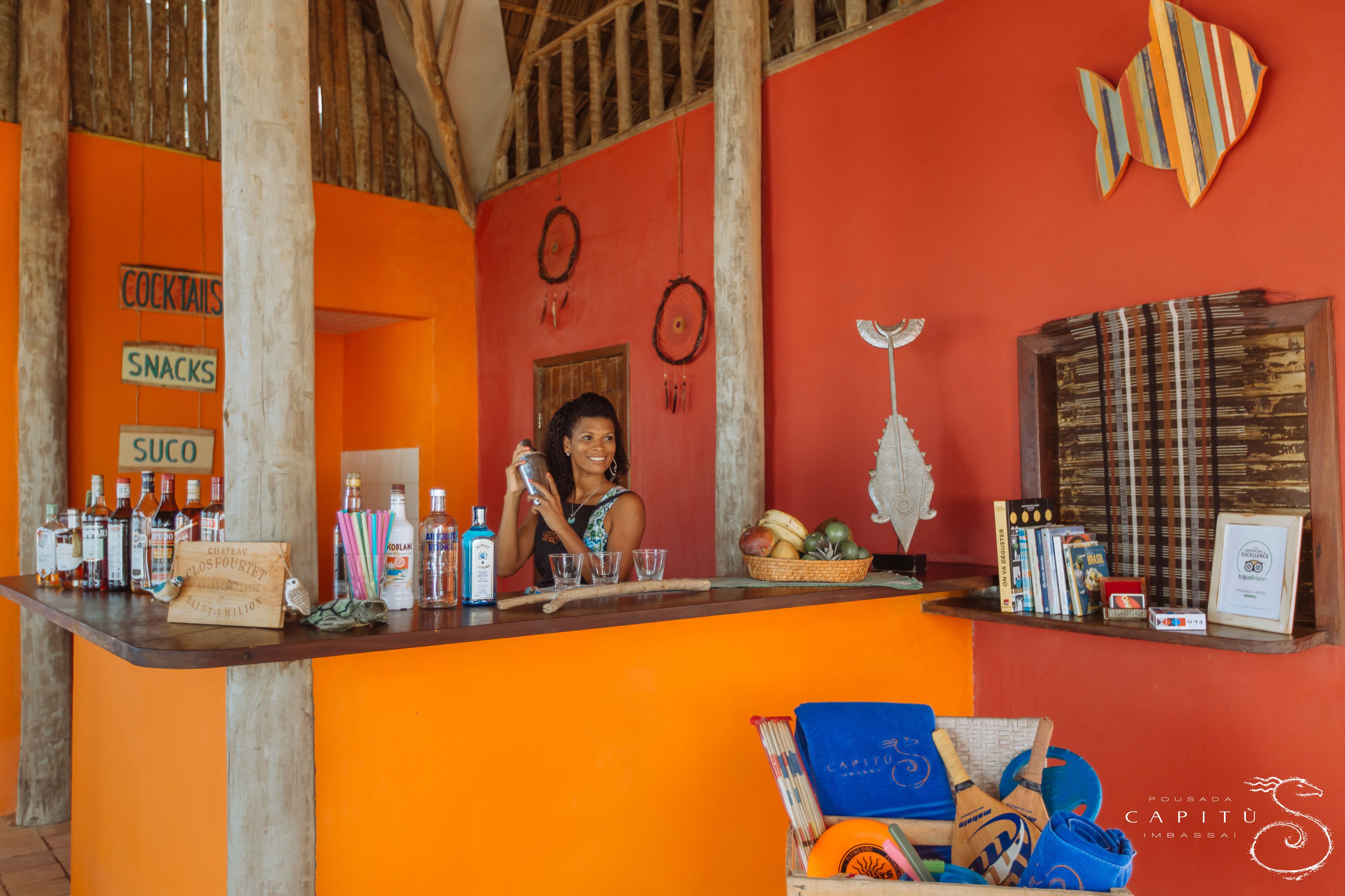 A bar area with a bartender, a sign listing cocktails, snacks, and sogo, and various bottles and glasses on the counter.