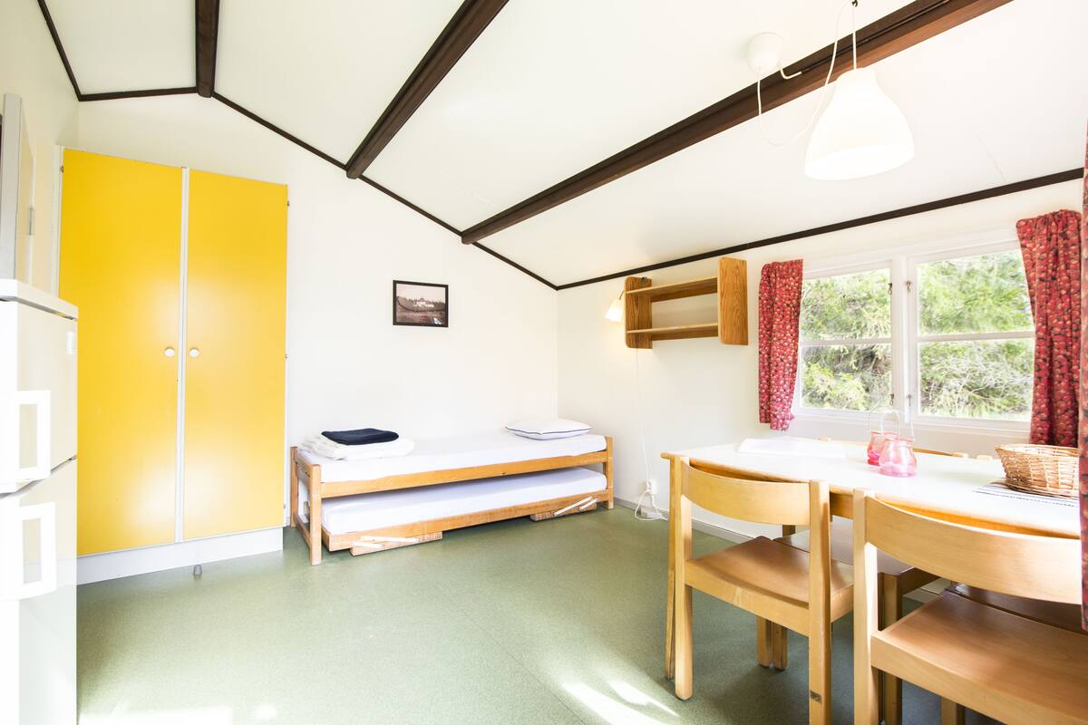 A room with a bed, a desk with a chair, a window with curtains, and a yellow wardrobe.