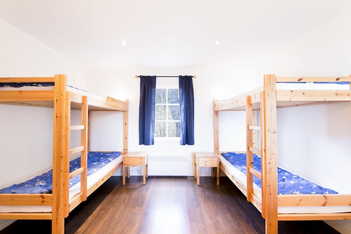 A room with two bunk beds, a small table, and a window with curtains.