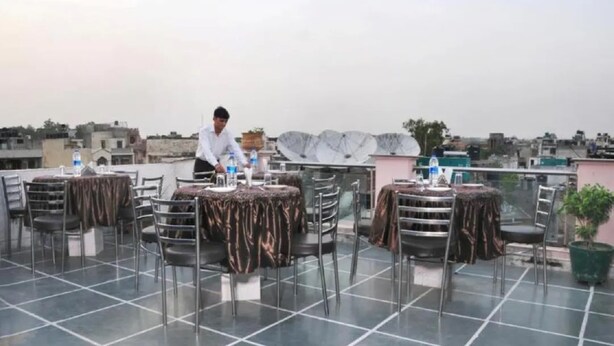 Ein Dachrestaurant mit gedeckten Tischen für Gäste, ein Kellner bedient ein Tisch, und dahinter sind Satellitenschüsseln zu sehen.