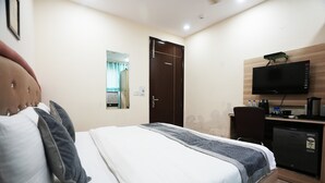 Ein Hotelzimmer mit Bett, Wandfernseher, kleinem Kühlschrank und Schreibtisch mit Wasserkocher und Tassen.