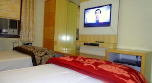 A hotel room with two beds, a television on the wall, and a wardrobe.