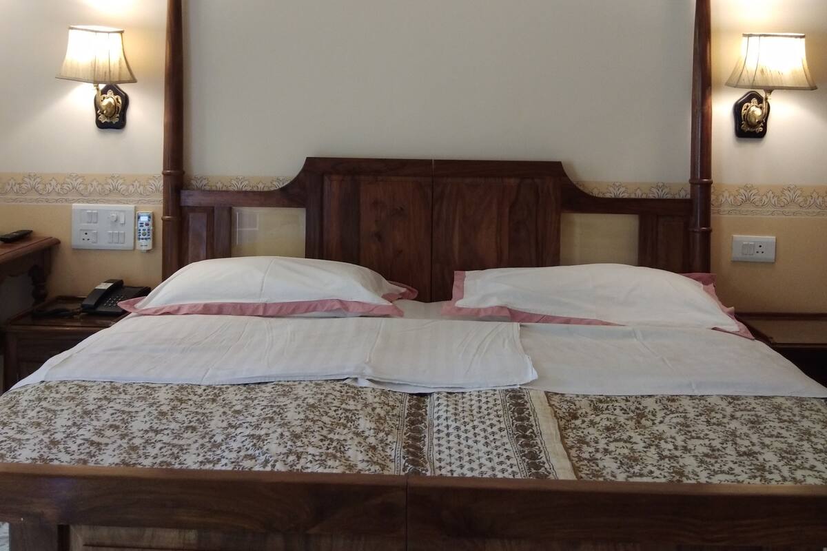 Ein Doppelbett mit Holz-Kopfstück, zwei Nachttische mit Lampen und eine zarte Bettdecke mit Blumenmuster.