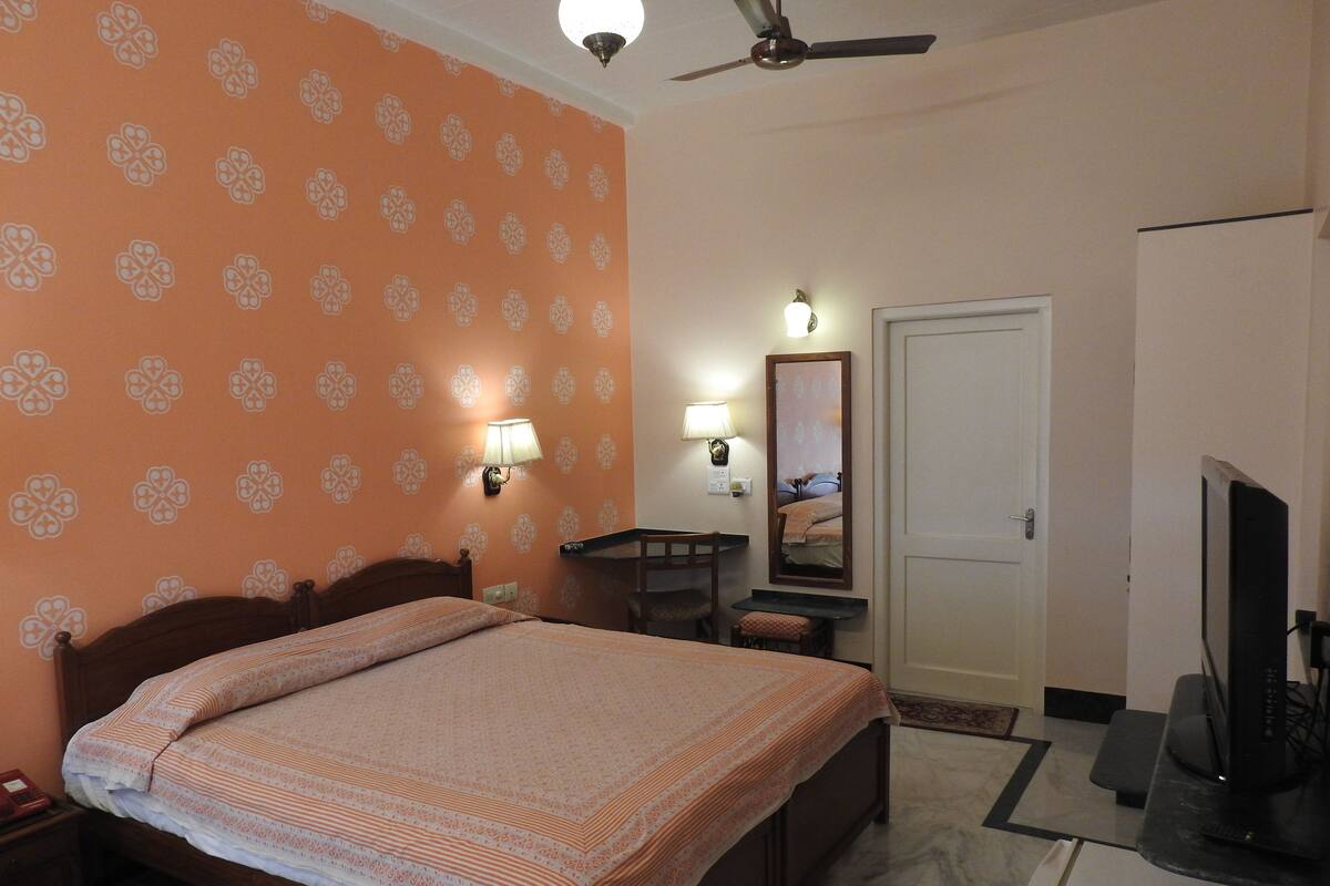 Ein Hotelzimmer mit Bett, Nachttisch, Lampe, Spiegel, Schreibtisch, Stuhl und Fernseher.